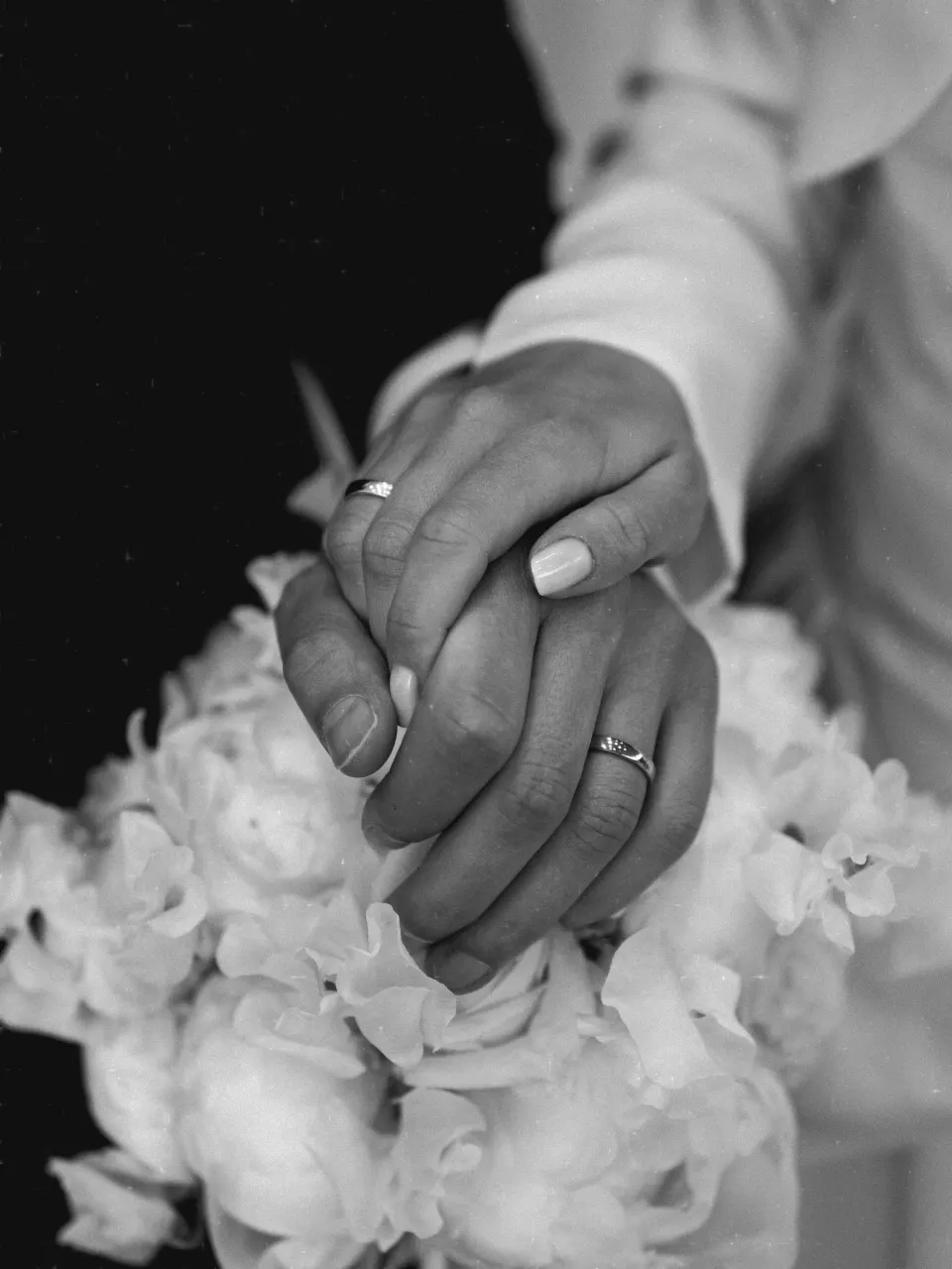 Hands with wedding ring resting on peony bouquet