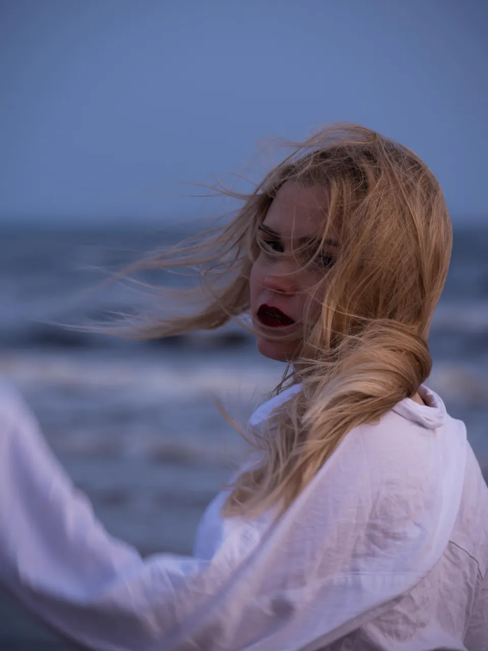 Editorial portrait with wind-blown hair by the sea at dusk